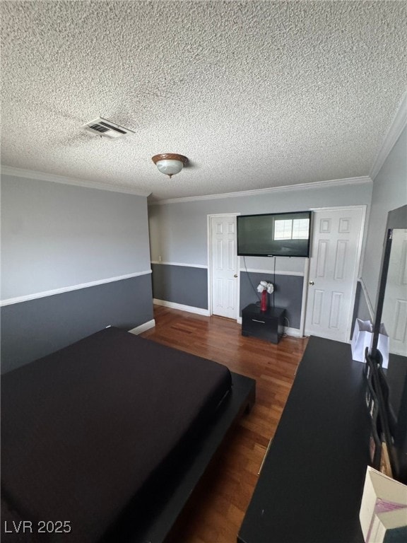 bedroom with wood finished floors, crown molding, a textured ceiling, visible vents, and baseboards