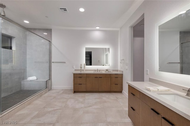 bathroom featuring baseboards, a shower stall, two vanities, and a sink