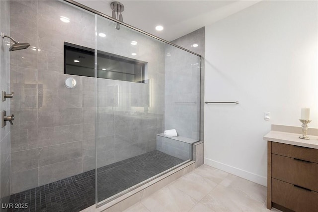 bathroom with a tile shower, baseboards, and vanity