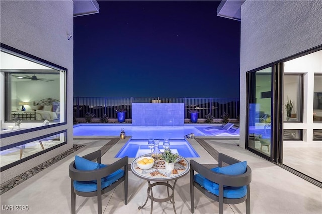 pool at night with a hot tub, fence, a patio, and a fenced in pool