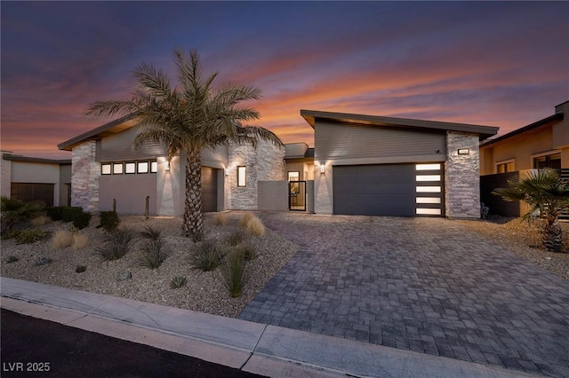 modern home featuring a garage, stucco siding, decorative driveway, and stone siding