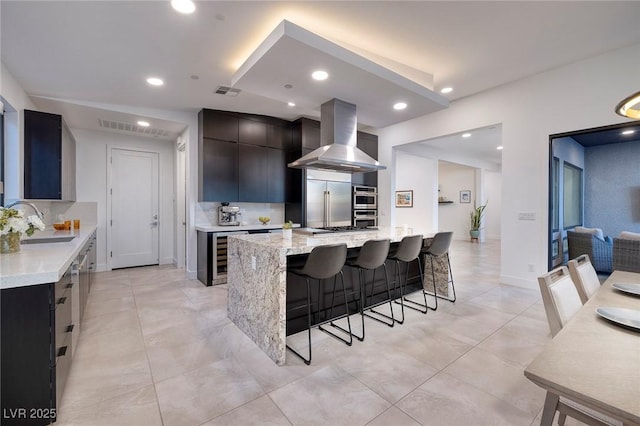 kitchen featuring a breakfast bar area, a sink, wall chimney range hood, appliances with stainless steel finishes, and recessed lighting