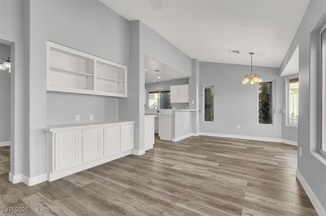 unfurnished living room with vaulted ceiling, baseboards, a chandelier, visible vents, and wood finished floors