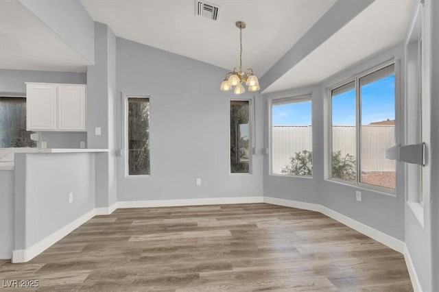 unfurnished dining area featuring lofted ceiling, baseboards, a chandelier, light wood finished floors, and visible vents