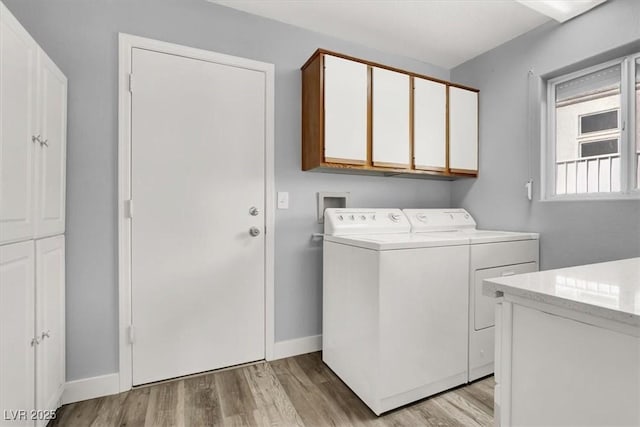 washroom with light wood finished floors, baseboards, washing machine and dryer, and cabinet space