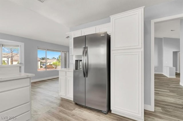 kitchen featuring light countertops, light wood finished floors, stainless steel fridge with ice dispenser, white cabinetry, and baseboards
