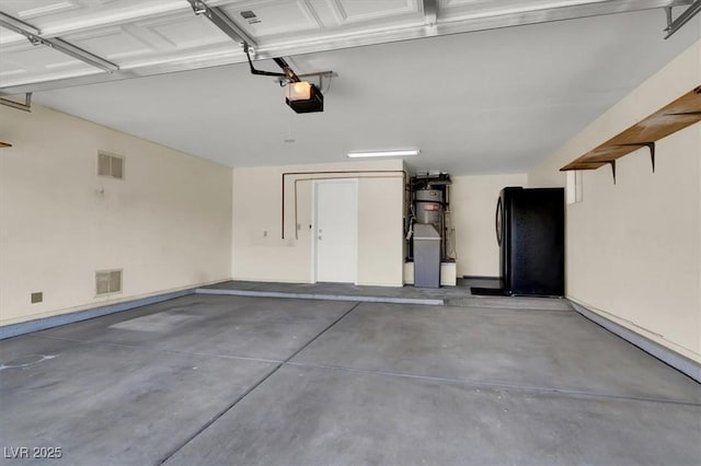 garage featuring a garage door opener, visible vents, baseboards, and freestanding refrigerator