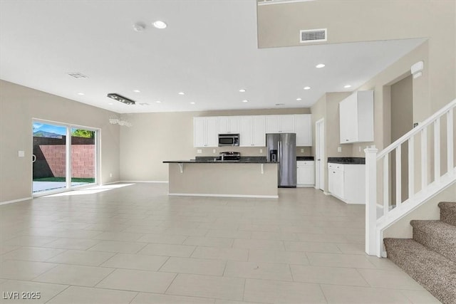 kitchen with white cabinets, visible vents, stainless steel appliances, dark countertops, and open floor plan