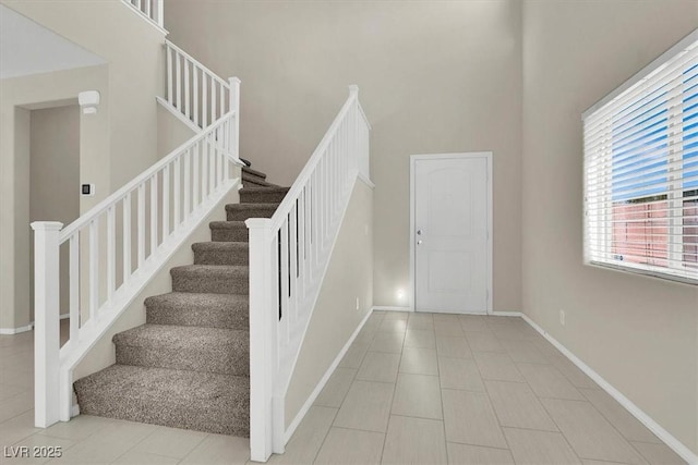 staircase with baseboards, a high ceiling, and tile patterned flooring