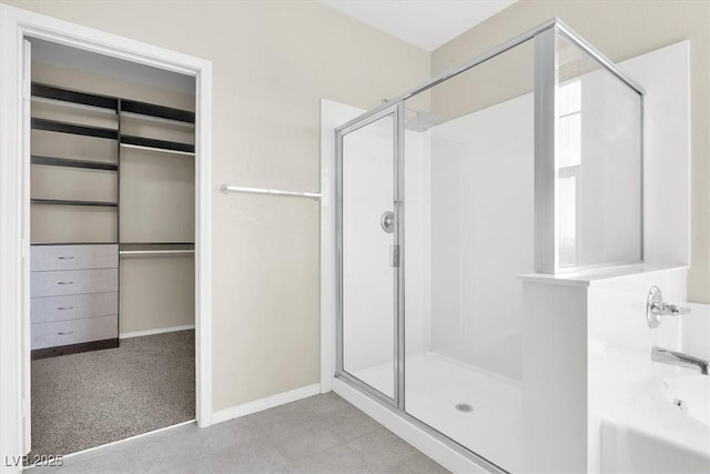 bathroom featuring a bath, a walk in closet, baseboards, and a shower stall
