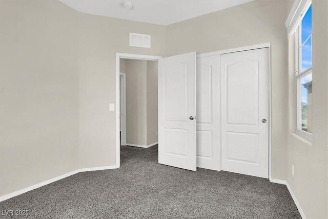 unfurnished bedroom with multiple windows, visible vents, dark carpet, and baseboards