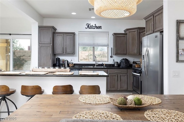 11913 Alava Ave, Las Vegas, NV 89138 - kitchen featuring stainless steel fridge, gas range oven, a breakfast bar area, dark countertops, and dark brown cabinetry