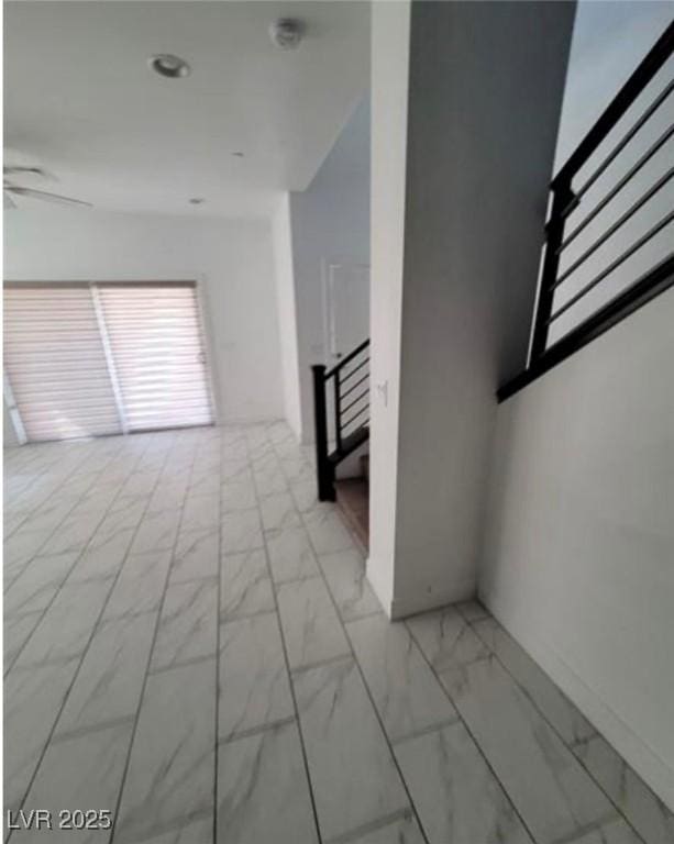 unfurnished room featuring marble finish floor, a ceiling fan, and stairs
