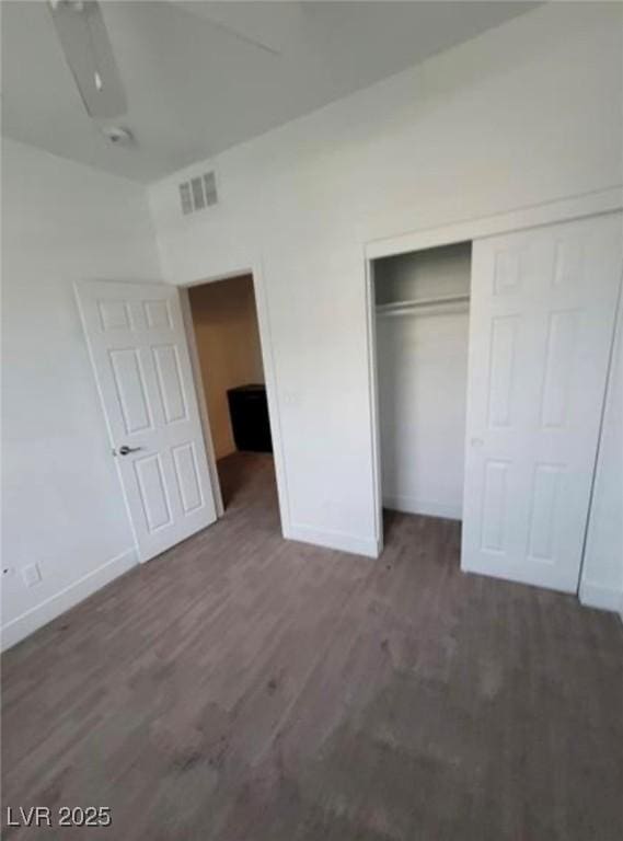 unfurnished bedroom featuring visible vents, a closet, baseboards, and wood finished floors