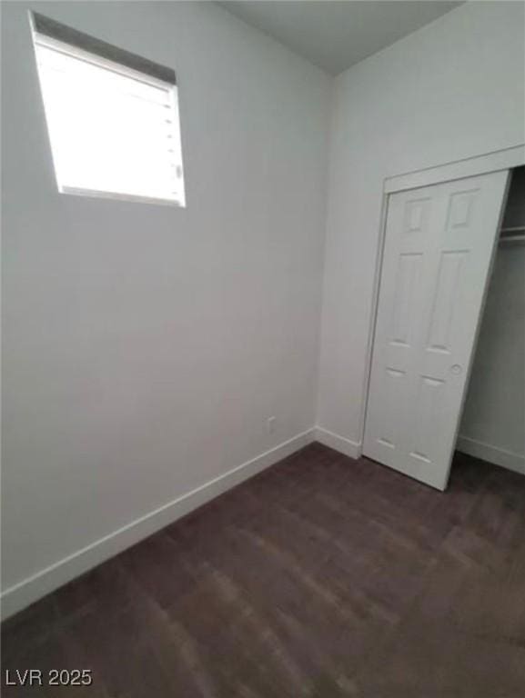 unfurnished bedroom featuring dark wood-type flooring, a closet, and baseboards