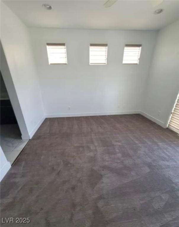 empty room featuring a wealth of natural light, dark colored carpet, and baseboards