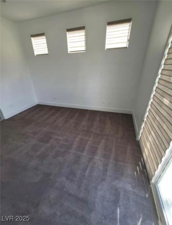 spare room featuring dark carpet and baseboards