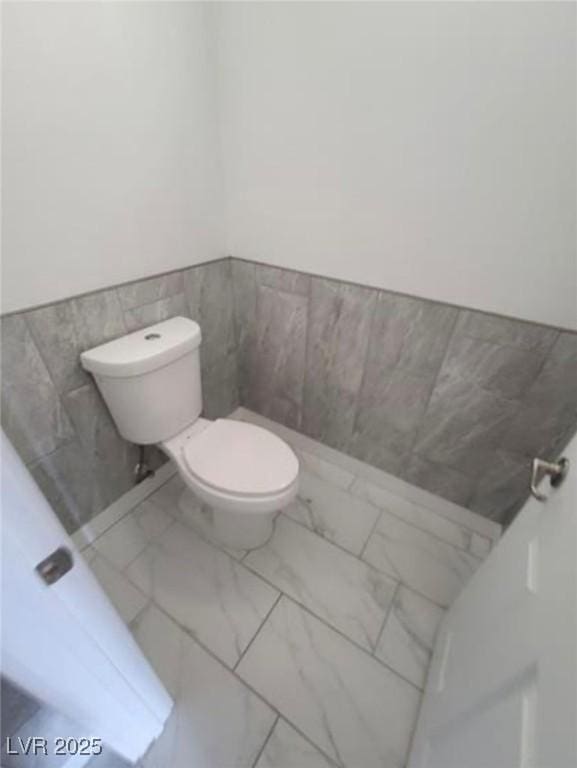bathroom with tile walls, toilet, marble finish floor, and a wainscoted wall