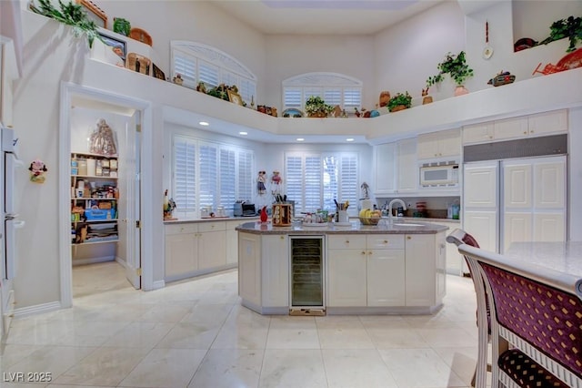 kitchen with a towering ceiling, a sink, white cabinets, beverage cooler, and built in appliances
