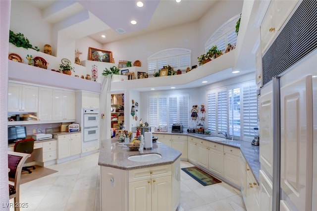 kitchen featuring a high ceiling, a sink, double oven, a center island, and paneled fridge