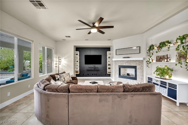 living room featuring a tiled fireplace, visible vents, light tile patterned flooring, and ceiling fan