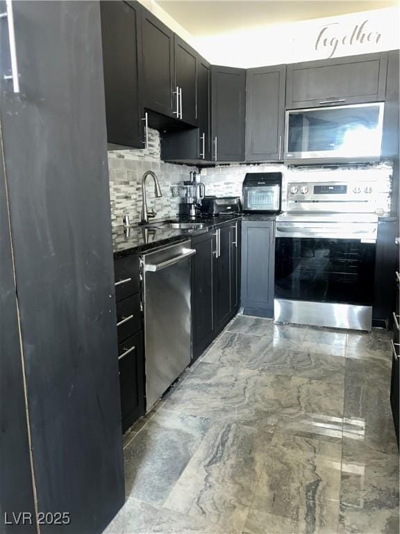 kitchen featuring dark stone counters, tasteful backsplash, a sink, marble finish floor, and appliances with stainless steel finishes