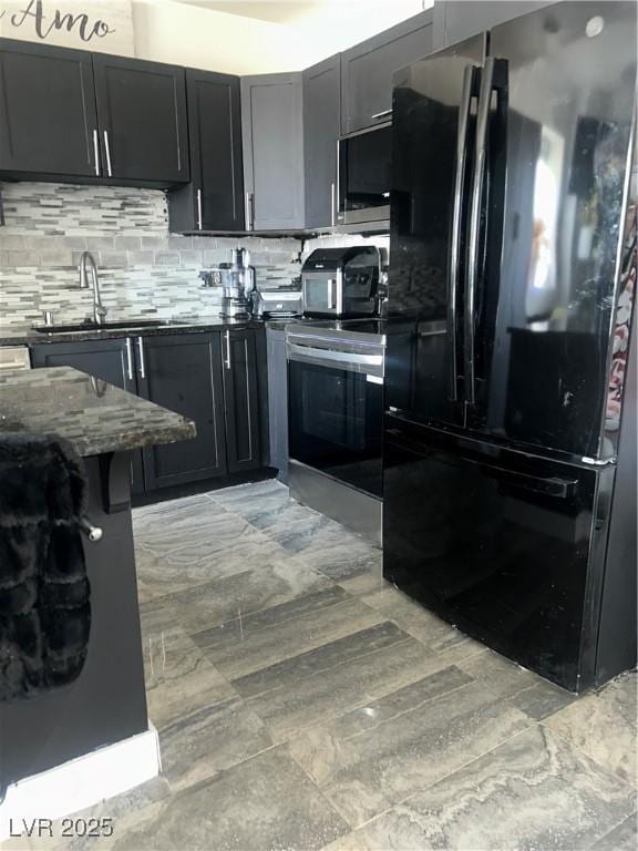 kitchen featuring stainless steel appliances, dark stone countertops, dark cabinetry, a sink, and decorative backsplash