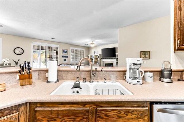 kitchen with a sink, open floor plan, dishwasher, ceiling fan, and a tile fireplace