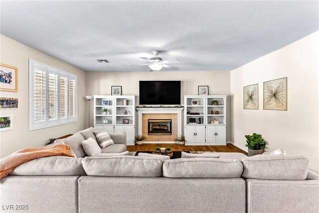 living area featuring wood finished floors, a tiled fireplace, a ceiling fan, and visible vents