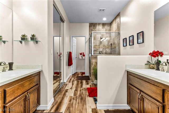 bathroom featuring a shower stall, two vanities, wood finished floors, and a sink