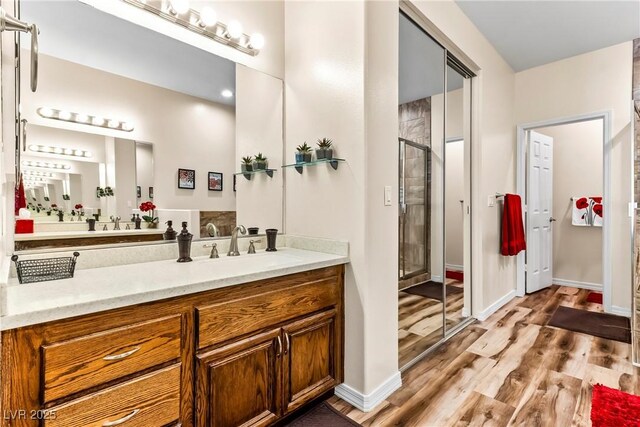 full bath with baseboards, vanity, wood finished floors, and a stall shower