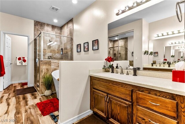 full bath featuring a freestanding bath, wood finished floors, visible vents, vanity, and a stall shower
