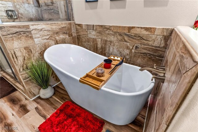 bathroom with a freestanding tub, tile walls, a wainscoted wall, and wood finished floors
