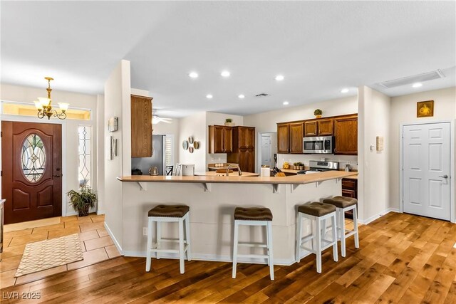kitchen featuring a peninsula, recessed lighting, light wood-style floors, a kitchen bar, and appliances with stainless steel finishes