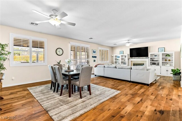 dining room with baseboards, visible vents, a ceiling fan, wood finished floors, and a fireplace