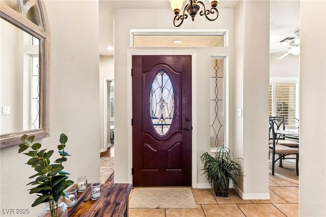 foyer featuring light tile patterned flooring and ceiling fan with notable chandelier