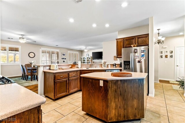 kitchen with a peninsula, a center island, stainless steel fridge, ceiling fan with notable chandelier, and light countertops