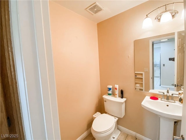 half bath with visible vents, baseboards, a sink, toilet, and tile patterned flooring