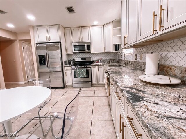 kitchen with visible vents, light tile patterned floors, a sink, light stone countertops, and stainless steel appliances