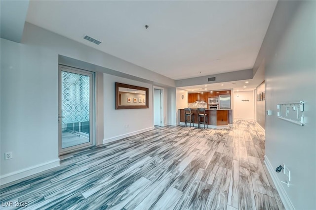 unfurnished living room featuring baseboards, light wood finished floors, and visible vents