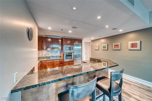 kitchen featuring a kitchen bar, visible vents, a sink, a peninsula, and built in appliances