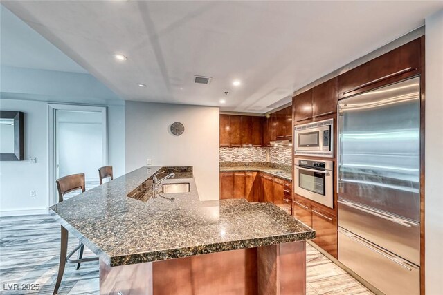kitchen featuring visible vents, a sink, a peninsula, built in appliances, and recessed lighting