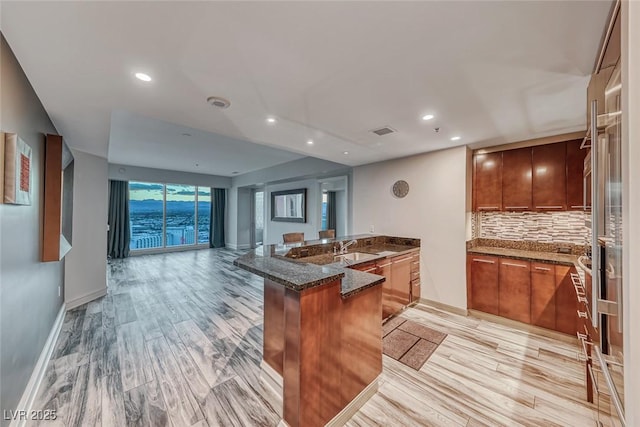 kitchen with brown cabinetry, visible vents, a sink, a peninsula, and dark stone counters