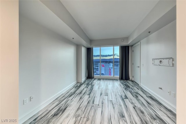empty room featuring light wood-type flooring, baseboards, a water view, and floor to ceiling windows