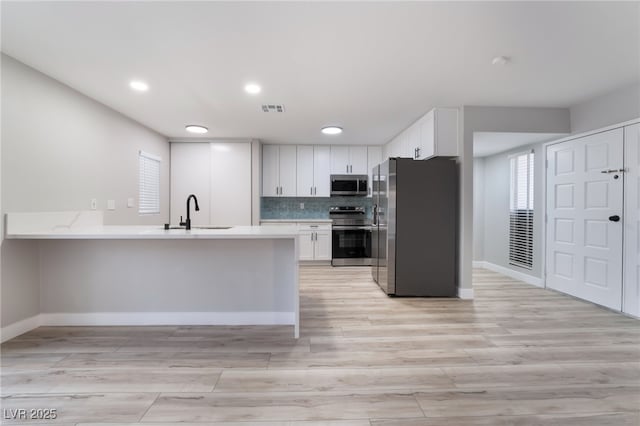 kitchen featuring visible vents, a sink, light countertops, a peninsula, and stainless steel appliances