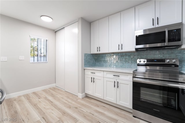 kitchen with tasteful backsplash, white cabinets, appliances with stainless steel finishes, and light wood-style floors
