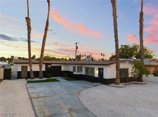 view of front facade featuring fence, driveway, stucco siding, and a gate