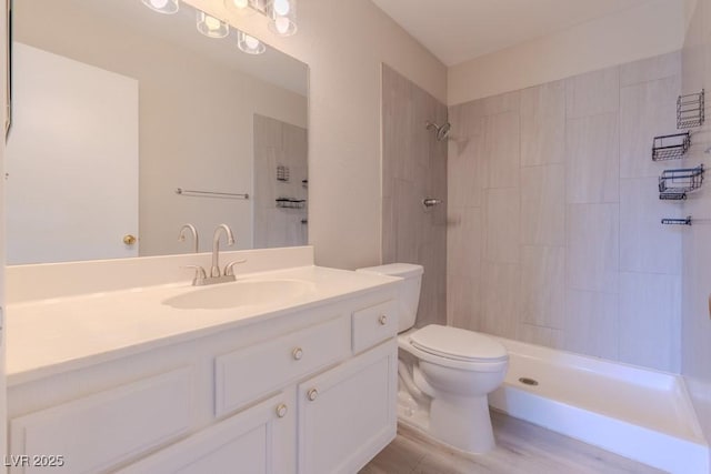 full bathroom featuring toilet, a tile shower, vanity, and wood finished floors