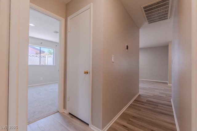 hallway with baseboards, visible vents, and wood finished floors