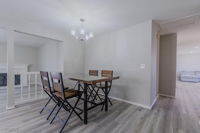 dining room with a chandelier, light wood-style flooring, baseboards, and a glass covered fireplace